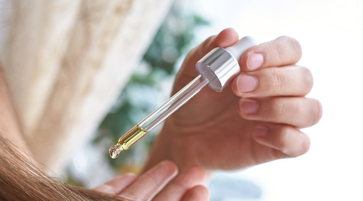 Jojobaöl tropft aus einer Pipette auf eine Handfläche